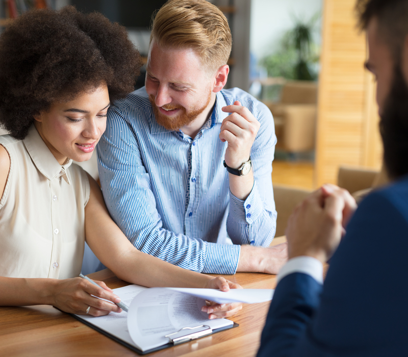 A young couple signing paperwork sat opposite a professional.