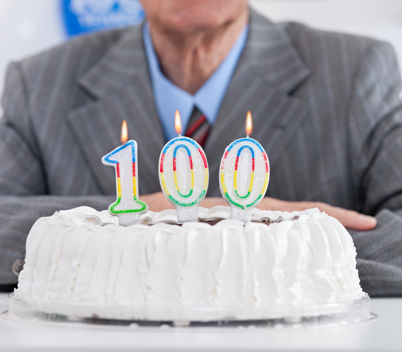 A man sitting behind a cake with “100” birthday candles.