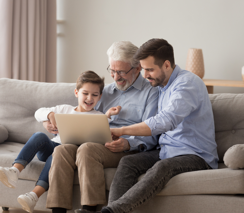 A grandfather using a laptop with his adult son and grandchild.