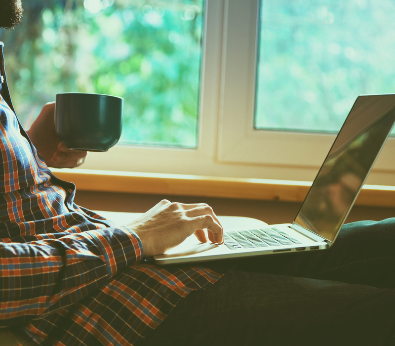 A man using a laptop and drinking a cup of tea.