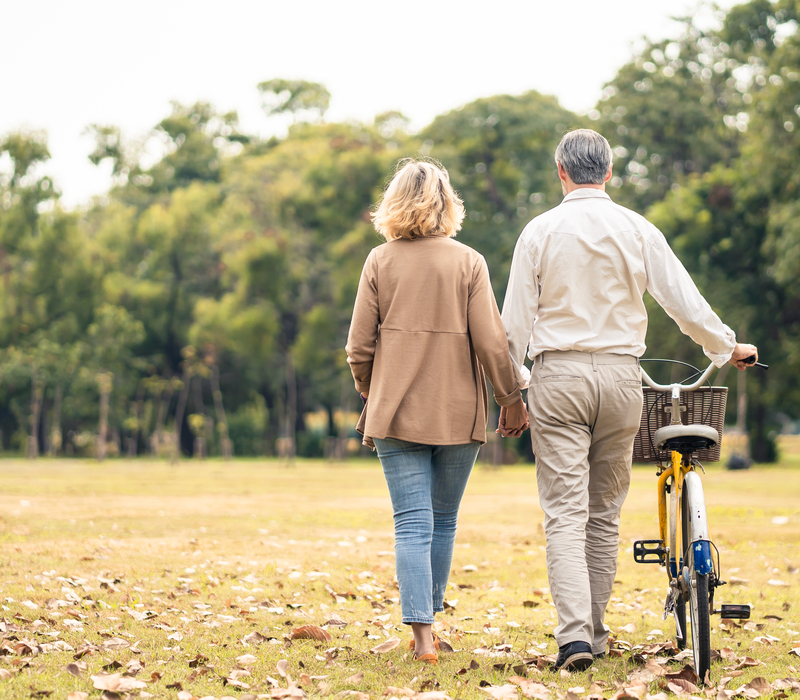 A couple walking through a park and pushing a bike.
