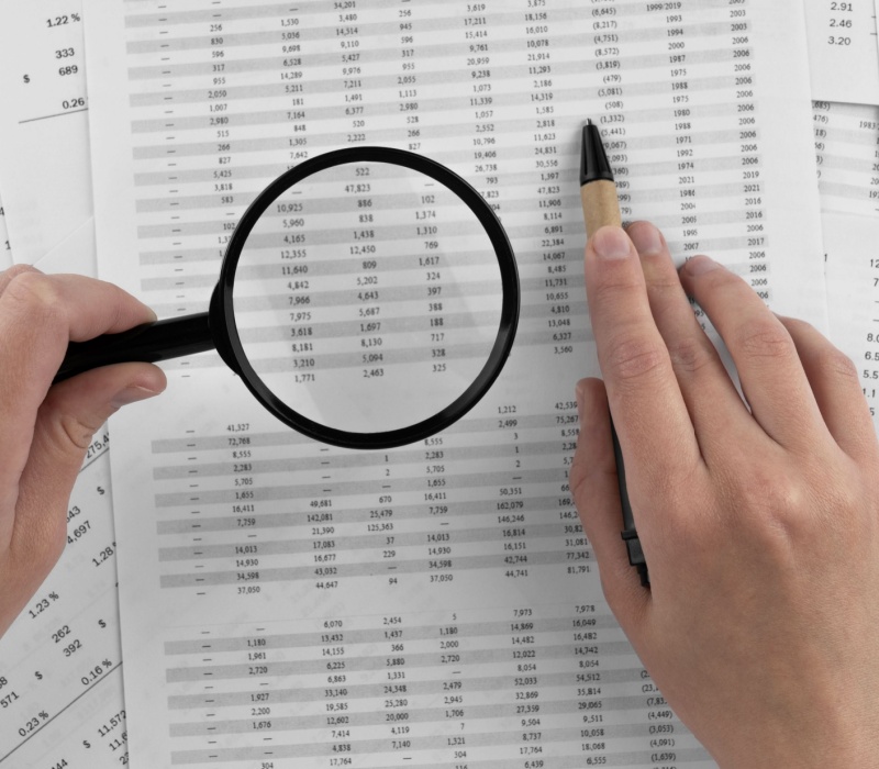 Somebody holding a magnifying glass to paperwork covered in numbers.